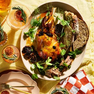 Slow-cooked l;amb shoulder recipe with black garlic and mint persillade on pink dish with white and orange check napkin and two grapefruit palomas with burnt grapefruit and a sprig of rosemary.