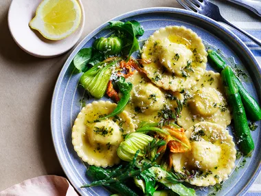 Spring ravioli with peas, ricotta and zucchini flowers on blue plate with slice of lemon.