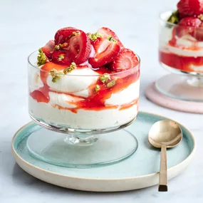 Strawberries with a pistachio crunch and mascarpone cream in a glass with a gold spoon.