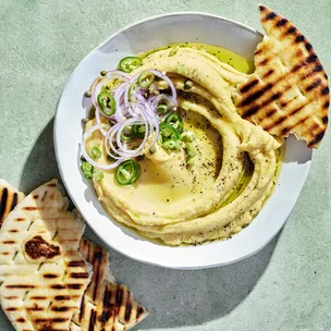 Yellow split pea dip with red onion, jalapeno and charred pita bread in white bowl.