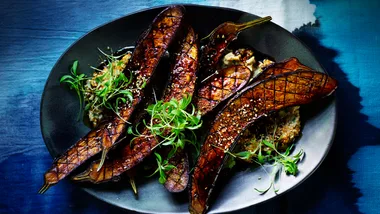 Four grilled Japanese eggplant slices, on a blue plate with a blue background.