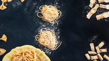 Types of pasta shapes, showcasing uncooked tagliolini, agnolotti del plin and farfalle pasta types on a dark coloured background