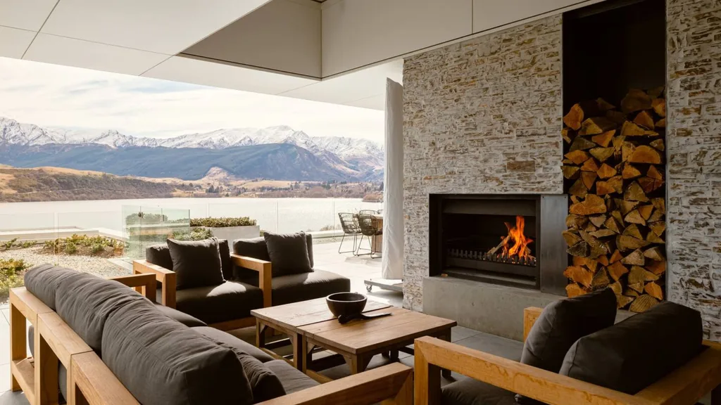 A photograph of a luxurious Queenstown airbnb with outdoor seats around a fireplace overlooking the mountain ranges.