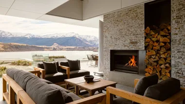 A photograph of a luxurious Queenstown airbnb with outdoor seats around a fireplace overlooking the mountain ranges.