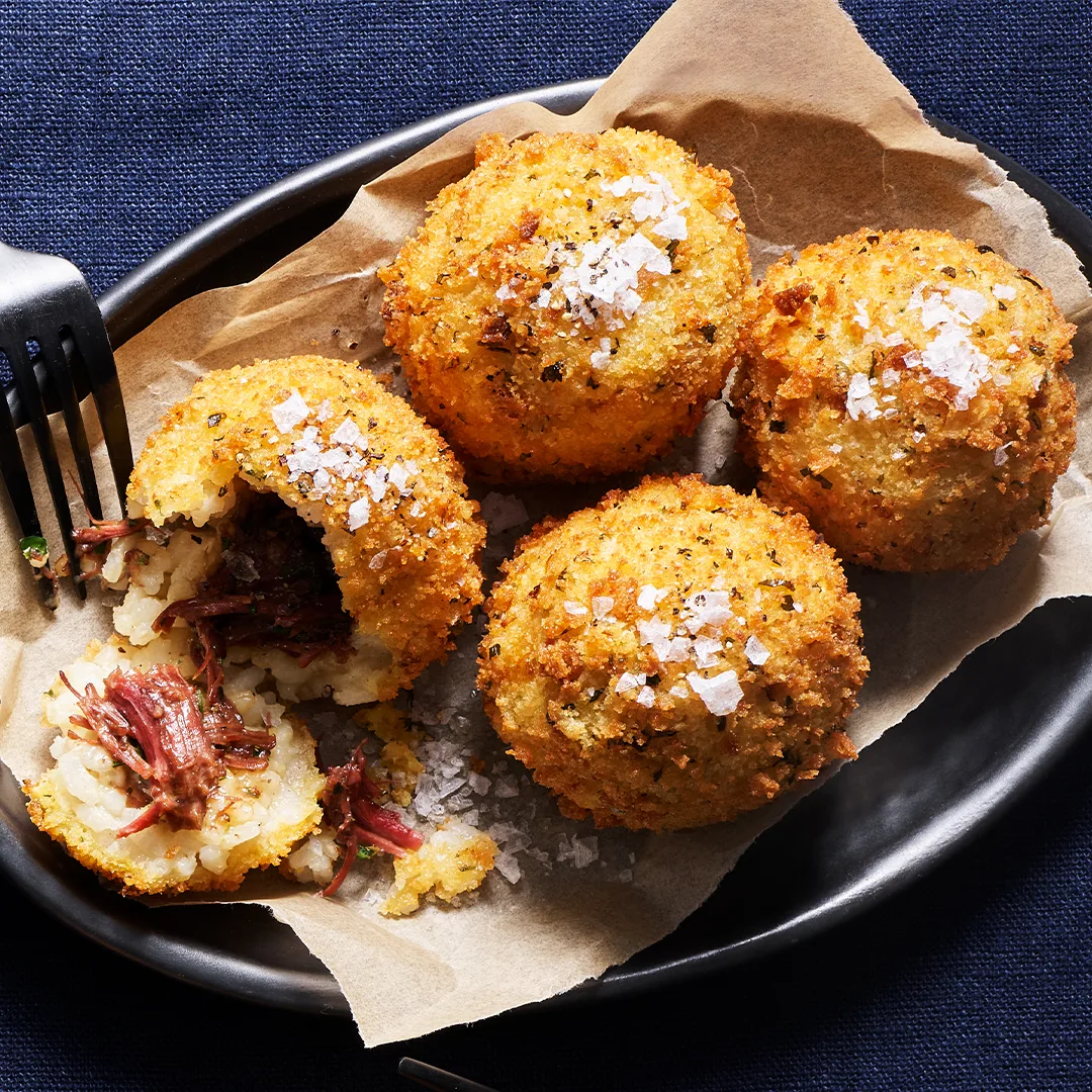 Four braised beef cheek arancini, one opened.