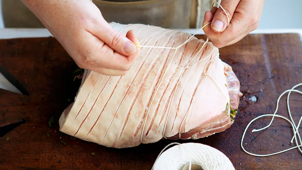 Porchetta is tied at intervals with kitchen string, then rubbed with oil and roasted.