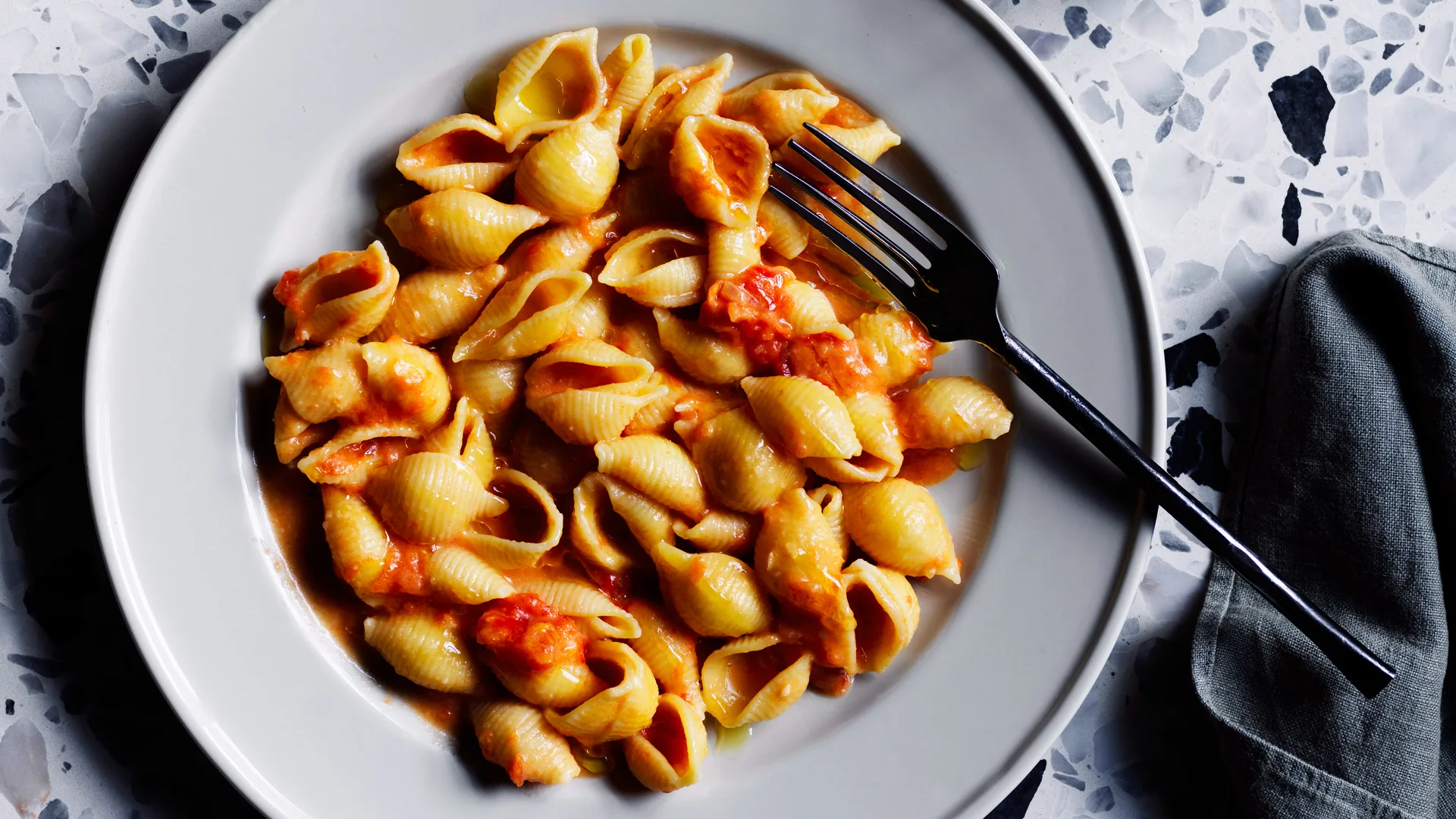 Conchiglie psta shape with bright red vodka sauce recipe in white boal and speckled stone background