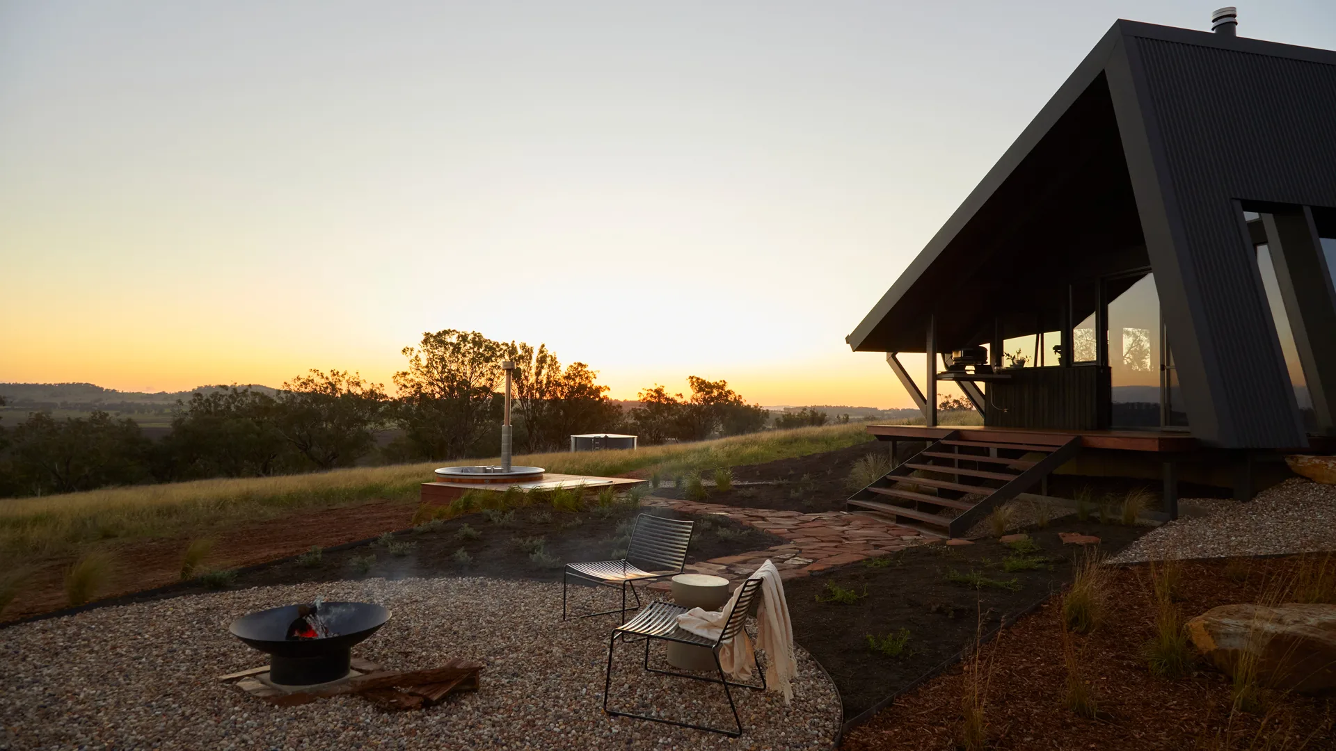 NSW tiny home stay Gilay Estate at sunset with lit outdoor fire pit, landscaped garden and hot tub