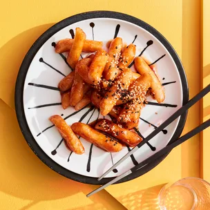 Tteokbokki recipe (Korean rice cakes) on white and black bowl with chopsticks on yellow background.