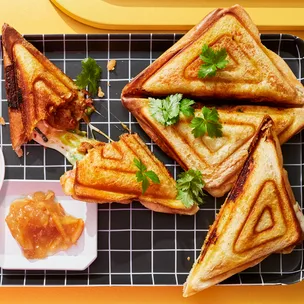 Korean spicy pork jaffle with orange marmalade on black grid tray.