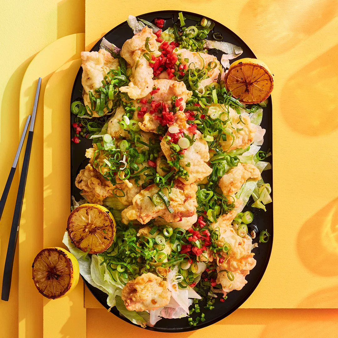 Lemon soy chicken with lemon wedges on a black platter, yellow background.