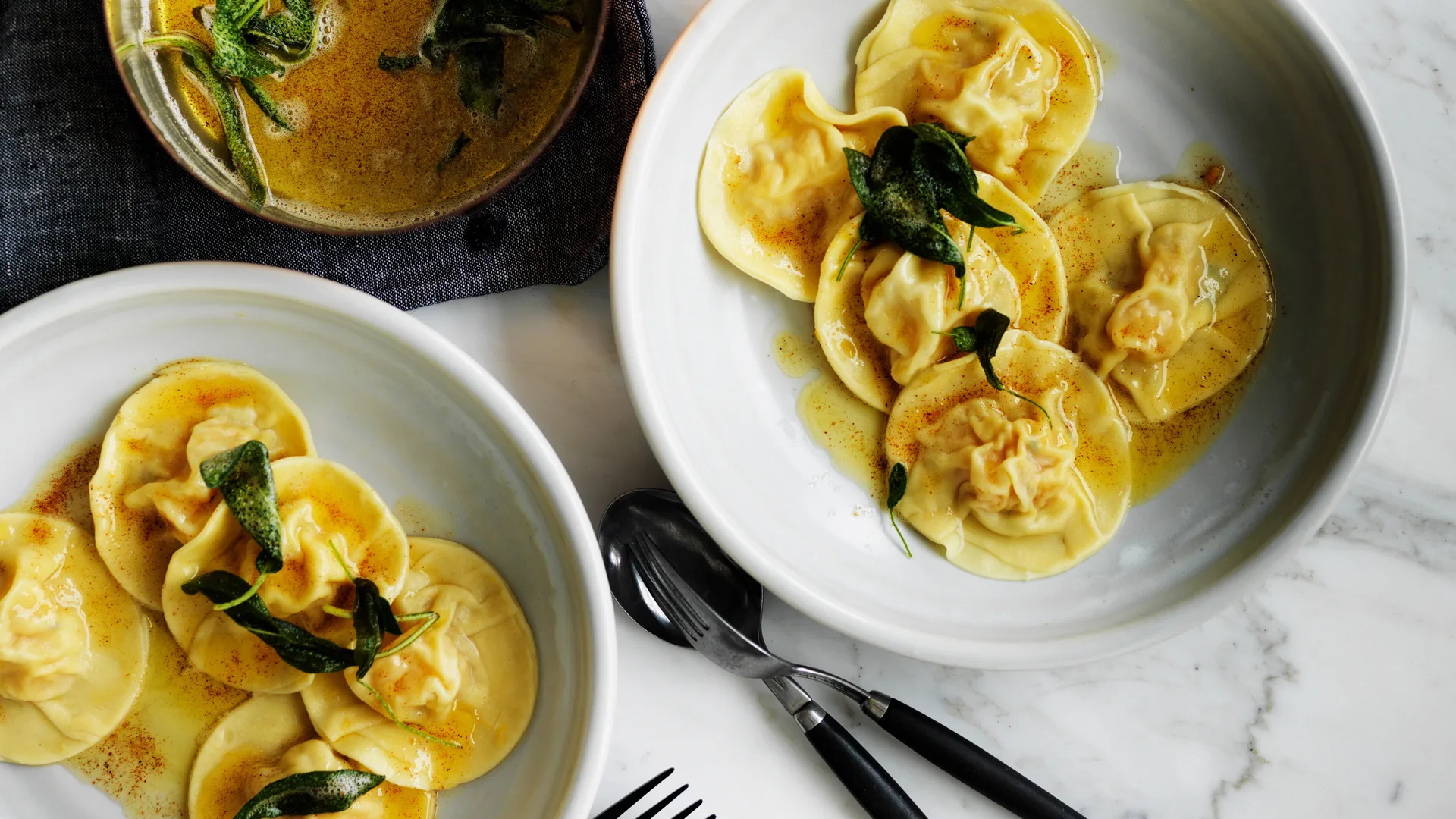 Two white bowls filled with circular pumpkin ravioli pasta with burnt butter and sage