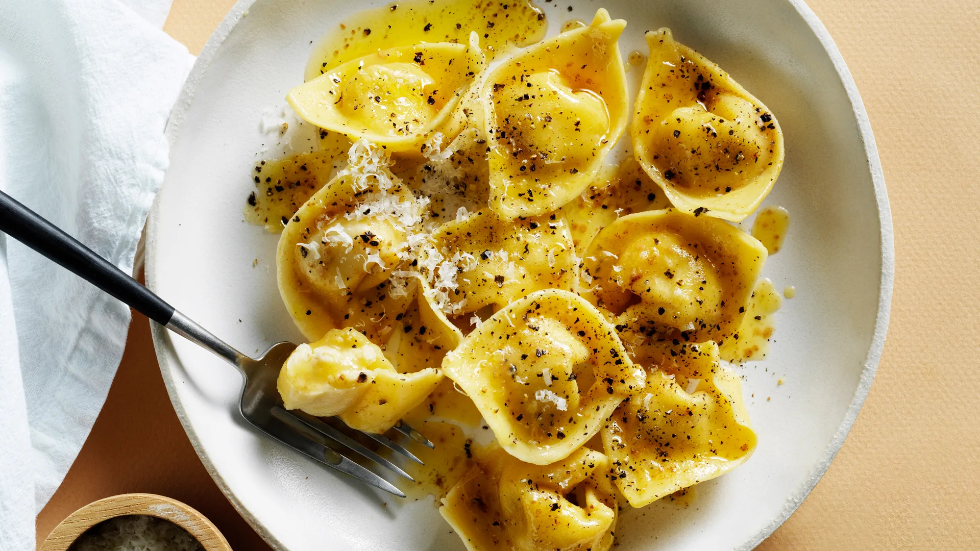 Close up photo of tortellini pasta with cacio e pepe showing cheese shavings and flecks of black pepper