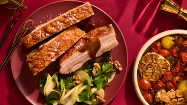 Twice-cooked pork belly roast with pickled apple salad and maple-glazed cabbage on red background.