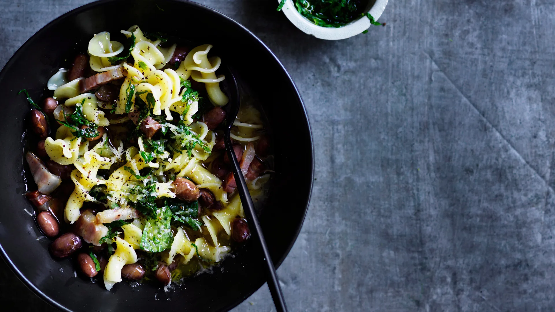 Pasta types: gigli pasta with pancetta and borlotti beans in black bowl against dark textured background