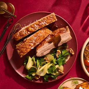 Twice-cooked pork belly with pickled apple salad and maple-glazed cabbage on red background.