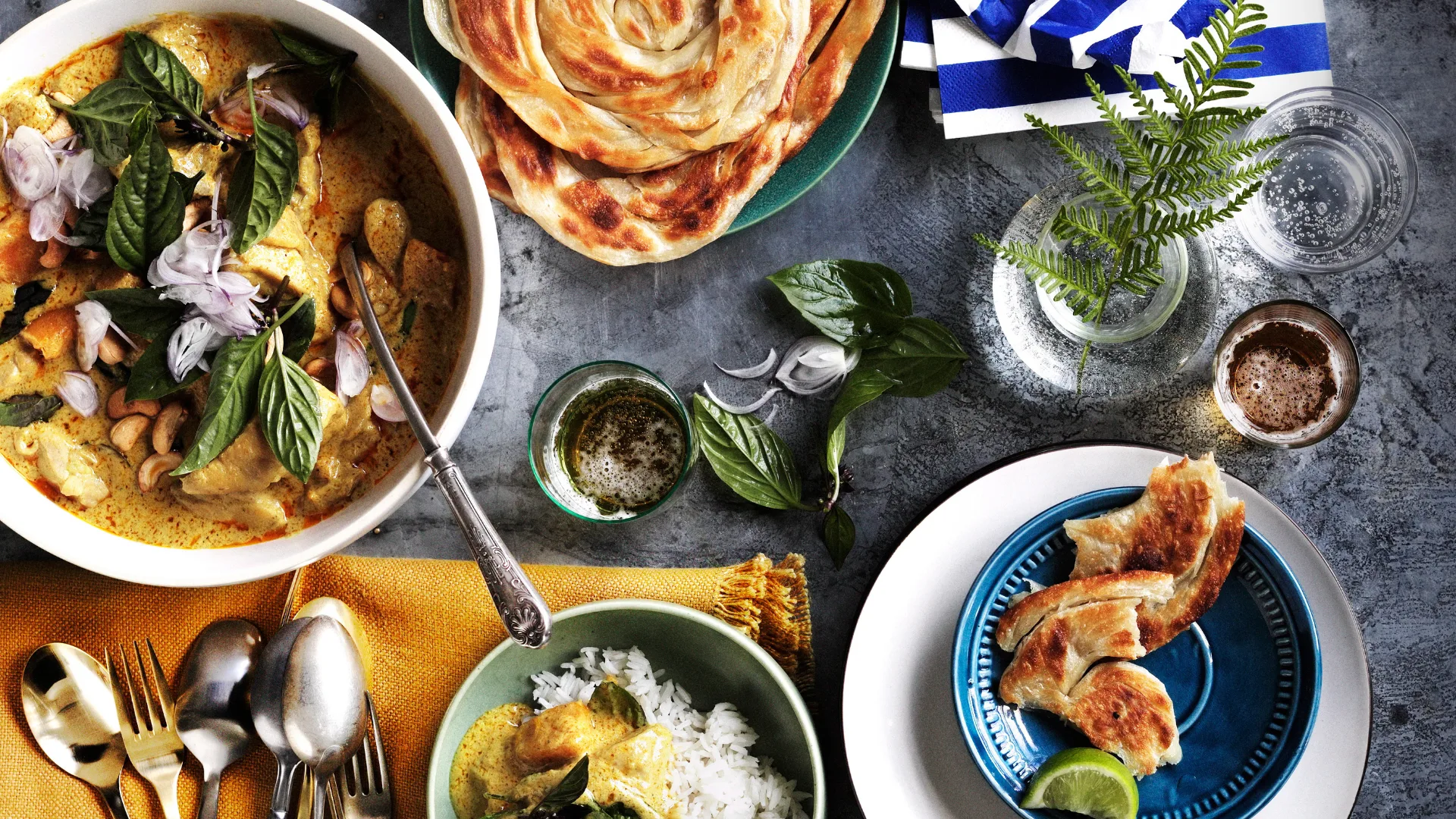 Thai chicken curry with roti with large bowl of chicken, smaller bowl with rice and curry and roti on plates.