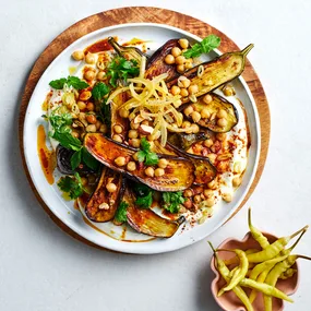 Chickpeas with steamed eggplant and harissa on white bowl with a pink bowl of guindilla chillies.