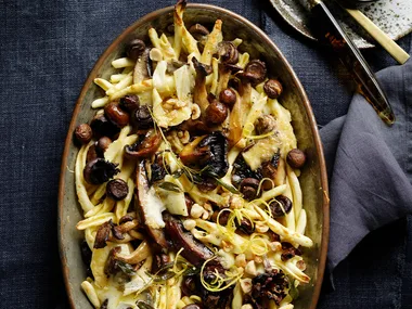 Mushroom and fontina maccheroni in serving dish on dark bacikground.