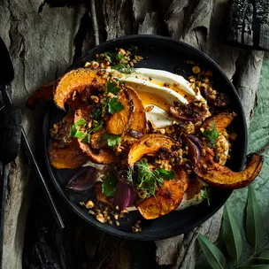 Roasted pumpkin, labneh and hazelnuts in black bowl on dark background.