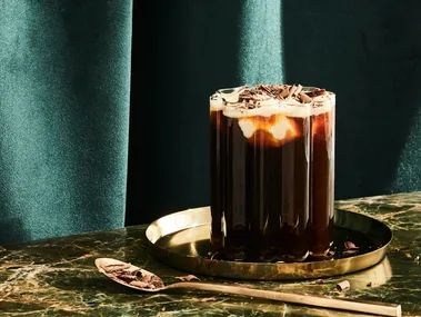 An Irish Coffee cocktail served in a clear ridged glass with an emerald green background