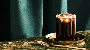 An Irish Coffee cocktail served in a clear ridged glass with an emerald green background