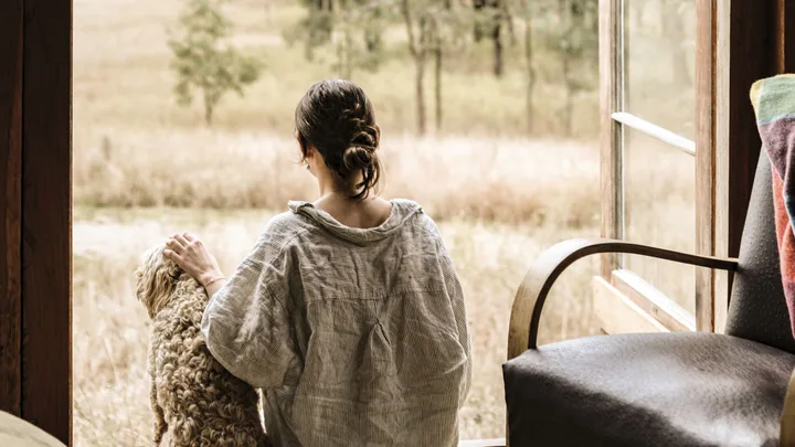 woman and a dog sit in a tiny cabin looking out to a field