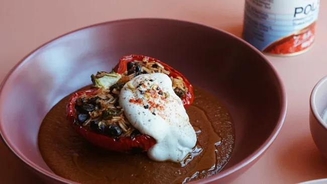 Stuffed red bell pepper with rice and beans, topped with cream and spices, served in a brown bowl.