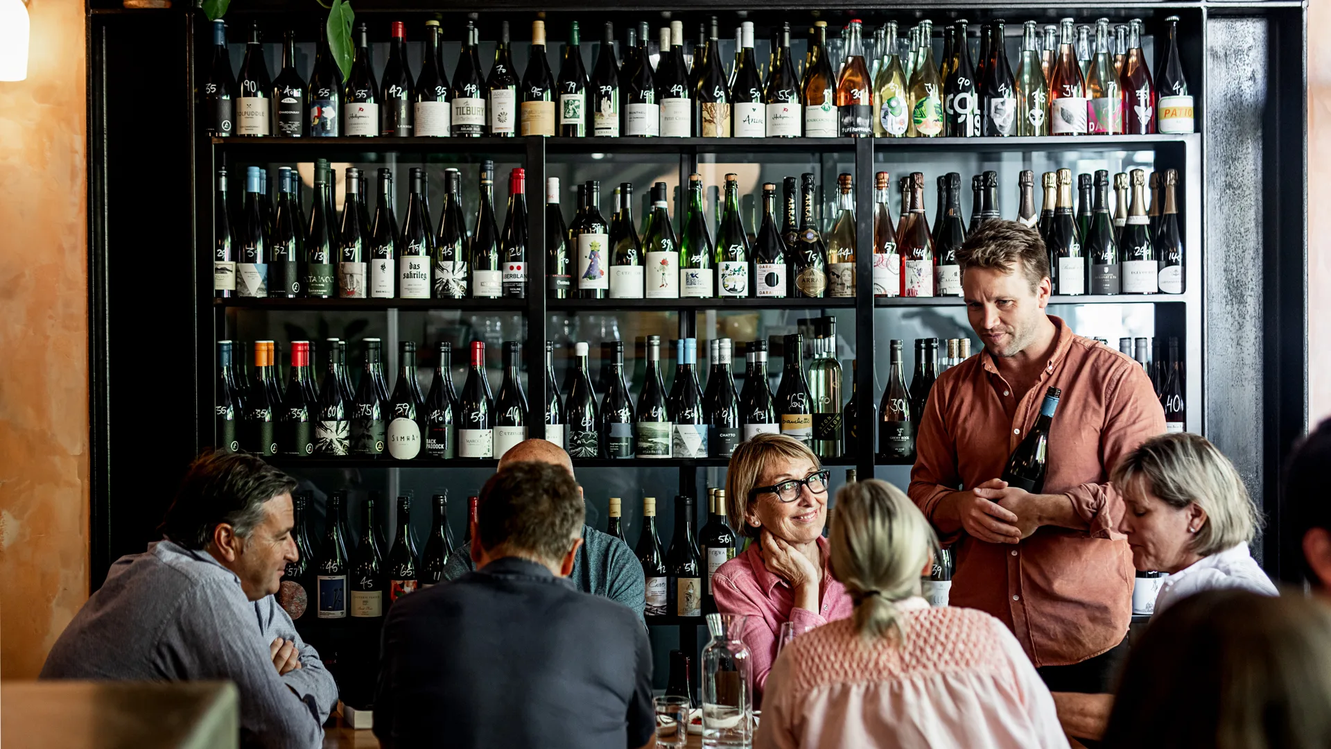 People sitting at a bar infront of a wall of wine