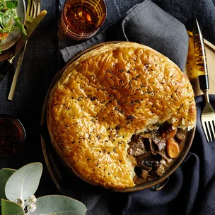 Kangaroo, ale and mushroom pie in ramekin on black background.