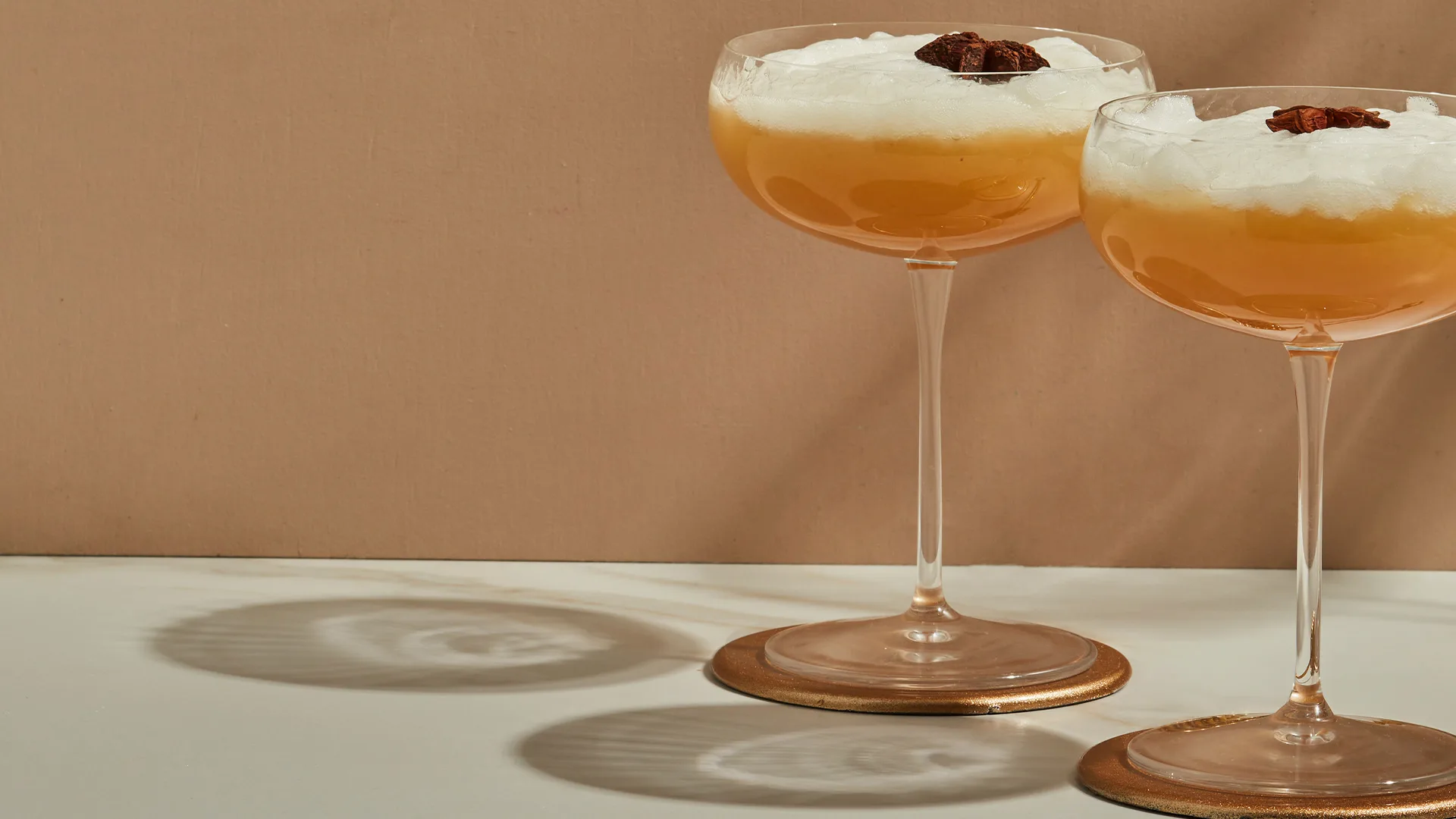 Two smoking camel cocktails garnished with star anise on rust backdrop.