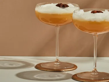 Two smoking camel cocktails garnished with star anise on rust backdrop.