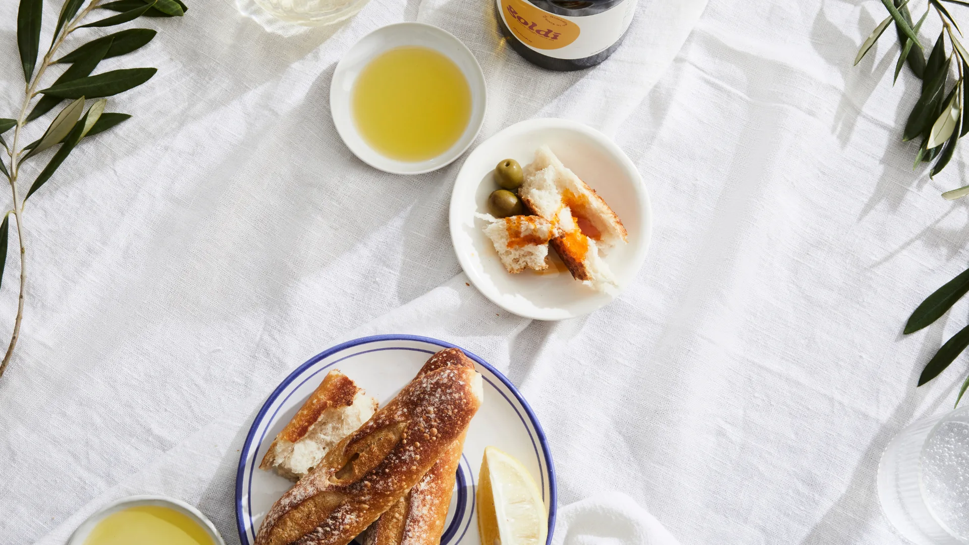 A white tablecloth with bread, oil and hummus.