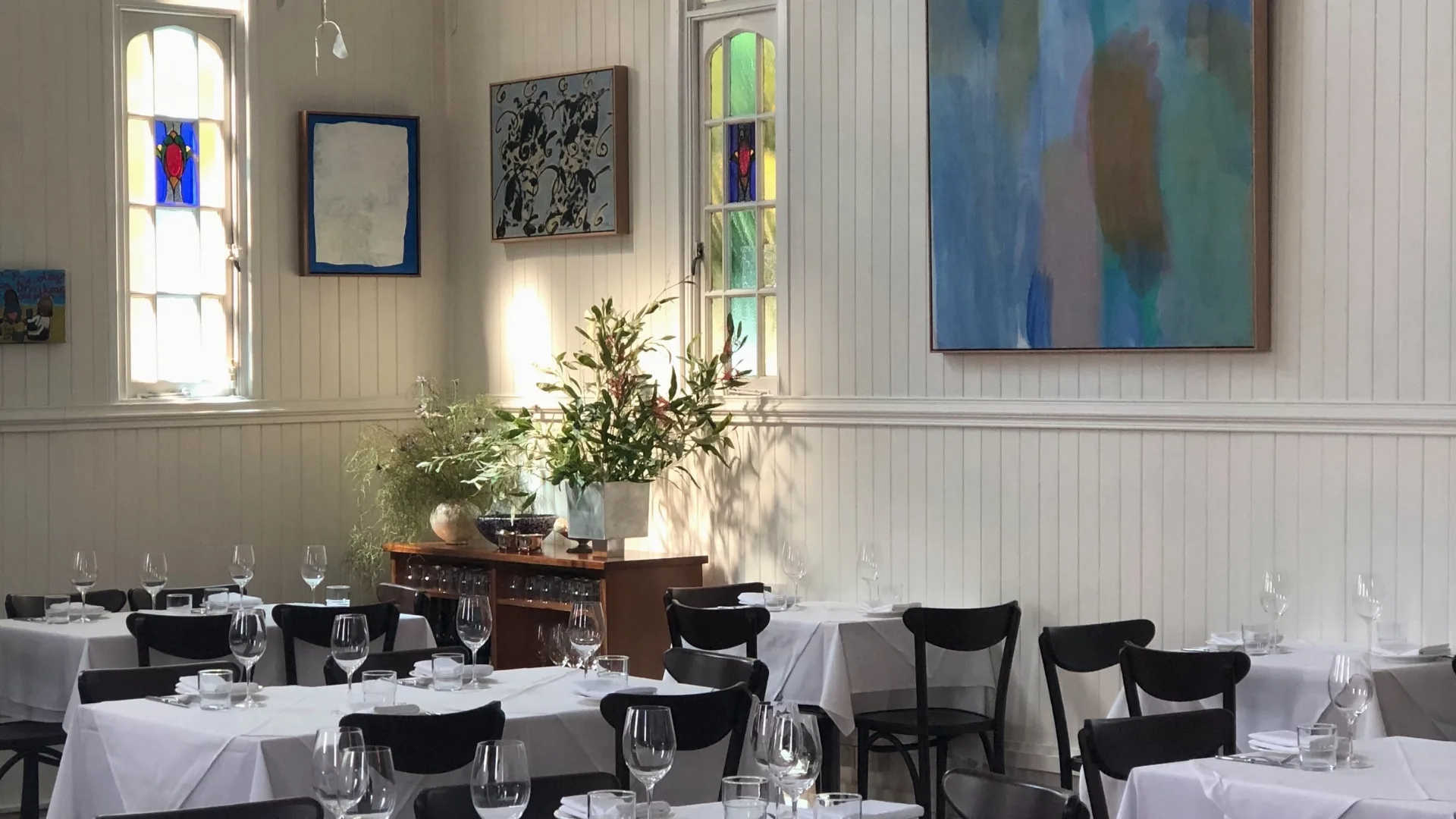  Art-covered timber walls and a white-tableclothed dining setting at August.