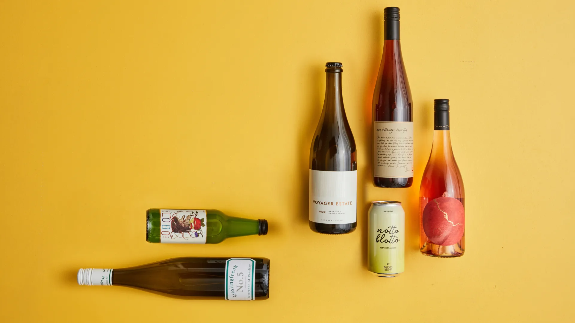 Five wine bottles and one can laid out against an orange background