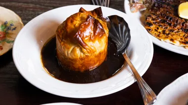 A cauliflower pie with gravy in a white bowl with a metal spoon.