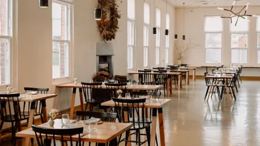 An empty dining room with wooden tables and black chairs.