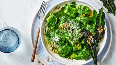 Ricotta gnocchi with cavolo nero and pine nuts with cutlery on blue serving plate.