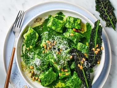 Ricotta gnocchi with cavolo nero and pine nuts with cutlery on blue serving plate.