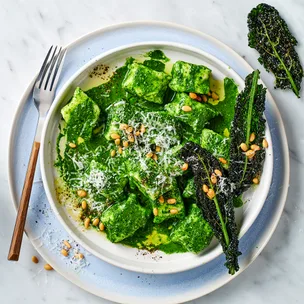 Ricotta gnocchi with cavolo nero and pine nuts with cutlery on blue serving plate.