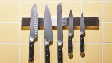 Kitchen knives hanging in a row against a yellow-tiled background