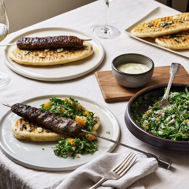 Lamb kofta with toum on tabletop with a tabbouleh side salad.