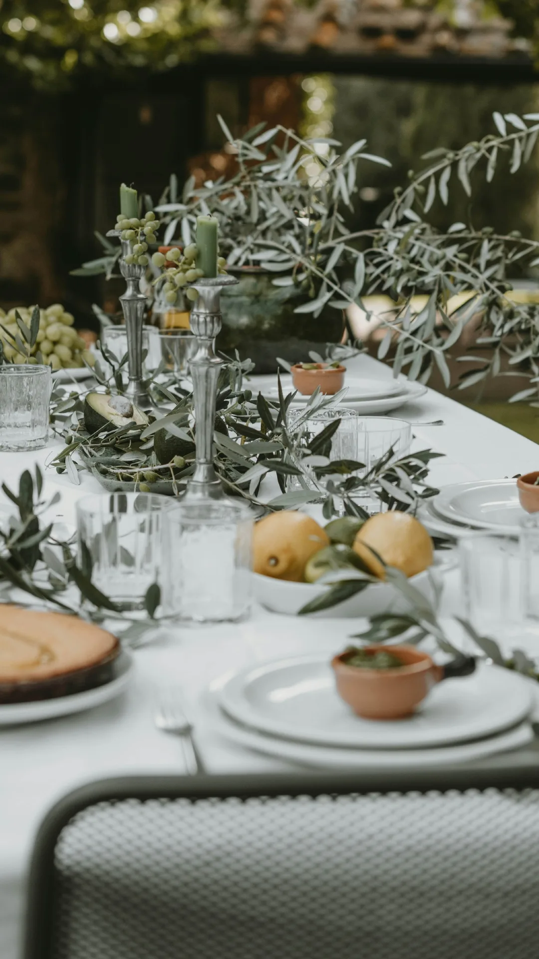 An outdoor dining table decorated with green candles and olive branches