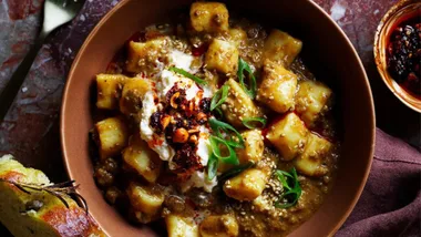 An overhead shot of a bowl of ricotta gnocchi in a mapo-inspired bolognese sauce with cutlery and charred bread