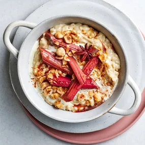 Coconut rice pudding with star anise and rhubarb in white ramekin on white and pink serving plates.