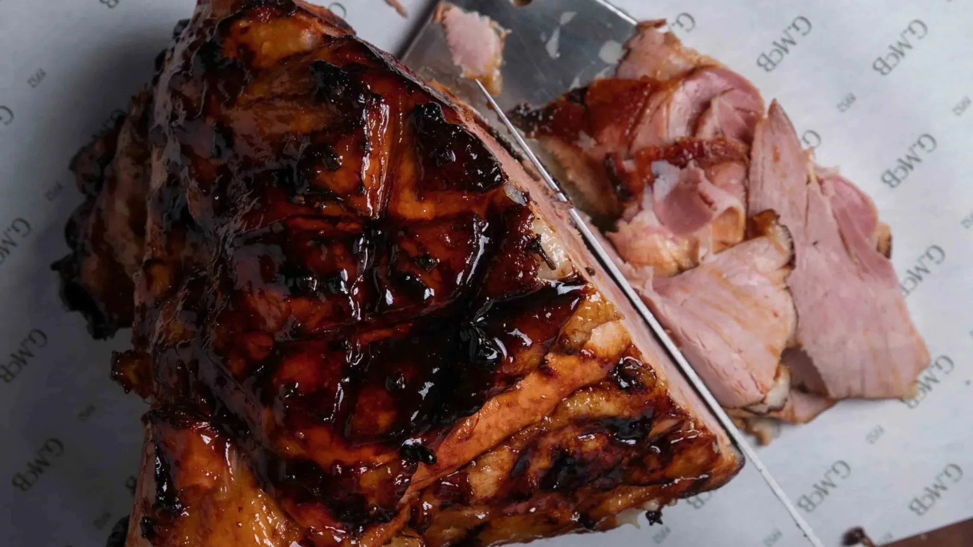 An overhead shot of a glossy, glazed ham being sliced
