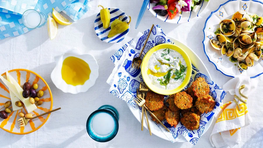 A table of greek recipes including greek salad, greek fritters and olives with white and blue plates