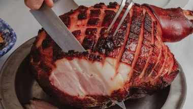 Picture of a ham being carved with sticky glaze and scored skin
