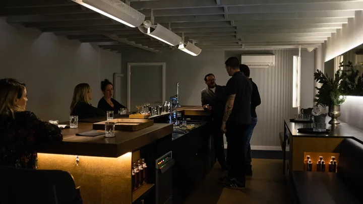 A dim-lit moody photograph of people standing around a bar table.