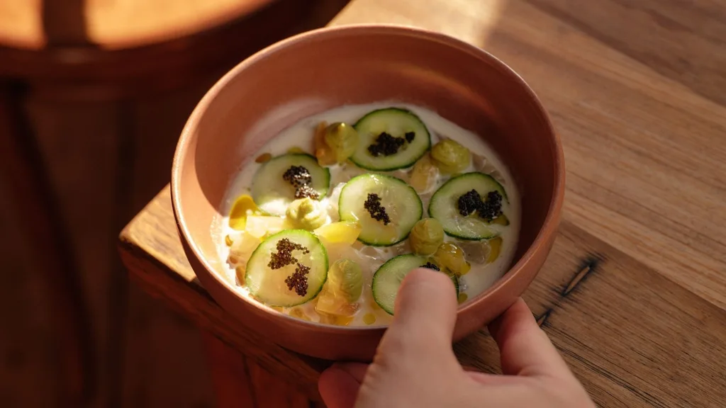 A close-up shot of Neighbourhood Wine's crudo, topped with thinly sliced cucumber and submerged in a ponzu, ginger sauce.